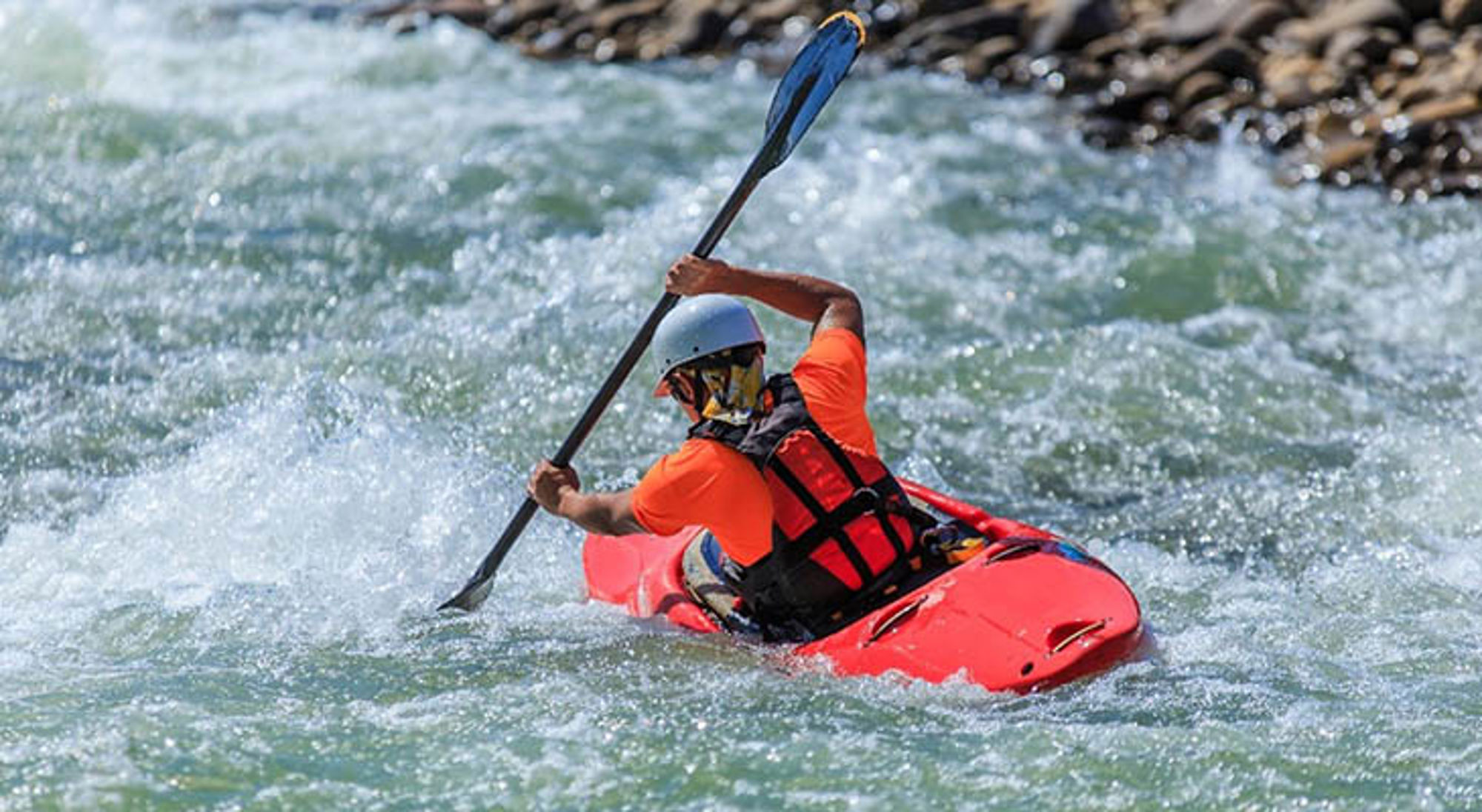 Raften Kajakker in rode kajak peddelt door wildwater op een rivier, met helm en reddingsvest.