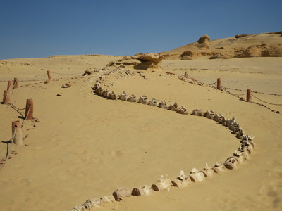 Zandduinen in de Egyptische woestijn met een slingerend pad van stenen en houten paaltjes.