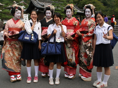 Japanse geisha’s in kleurrijke kimono’s poseren met scholieren op straat in Kyoto.