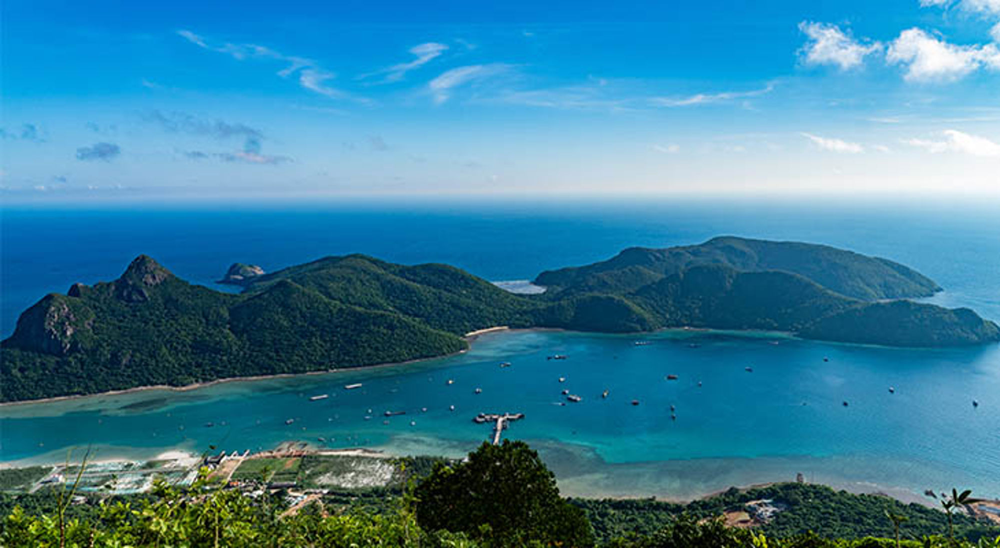 Con Dao Panoramisch uitzicht op een baai met groene heuvels en turquoise zee met bootjes in Vietnam.