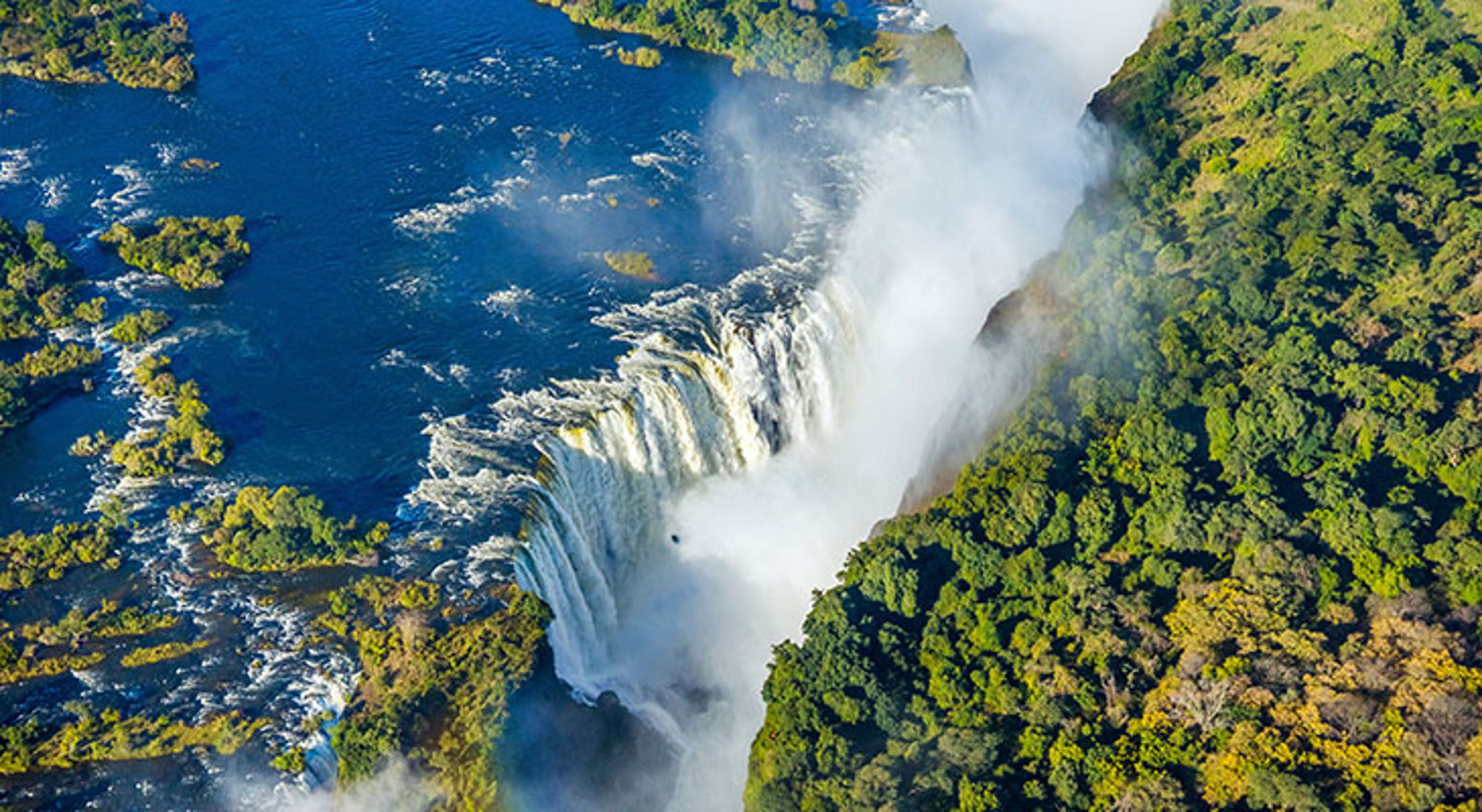 Victoria Falls Zimbabwe Zambia de Victoriawatervallen met opspattend water en groene rivieroevers.