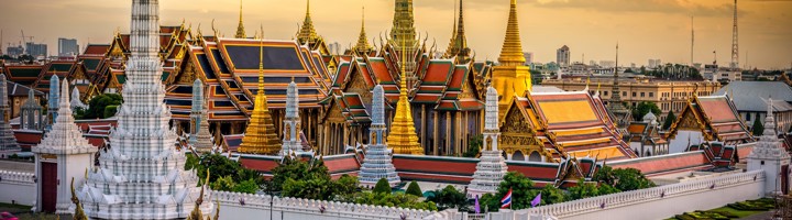 Wat Phra Kaew in Bangkok met gouden tempeltorens en kleurrijke daken bij zonsondergang.