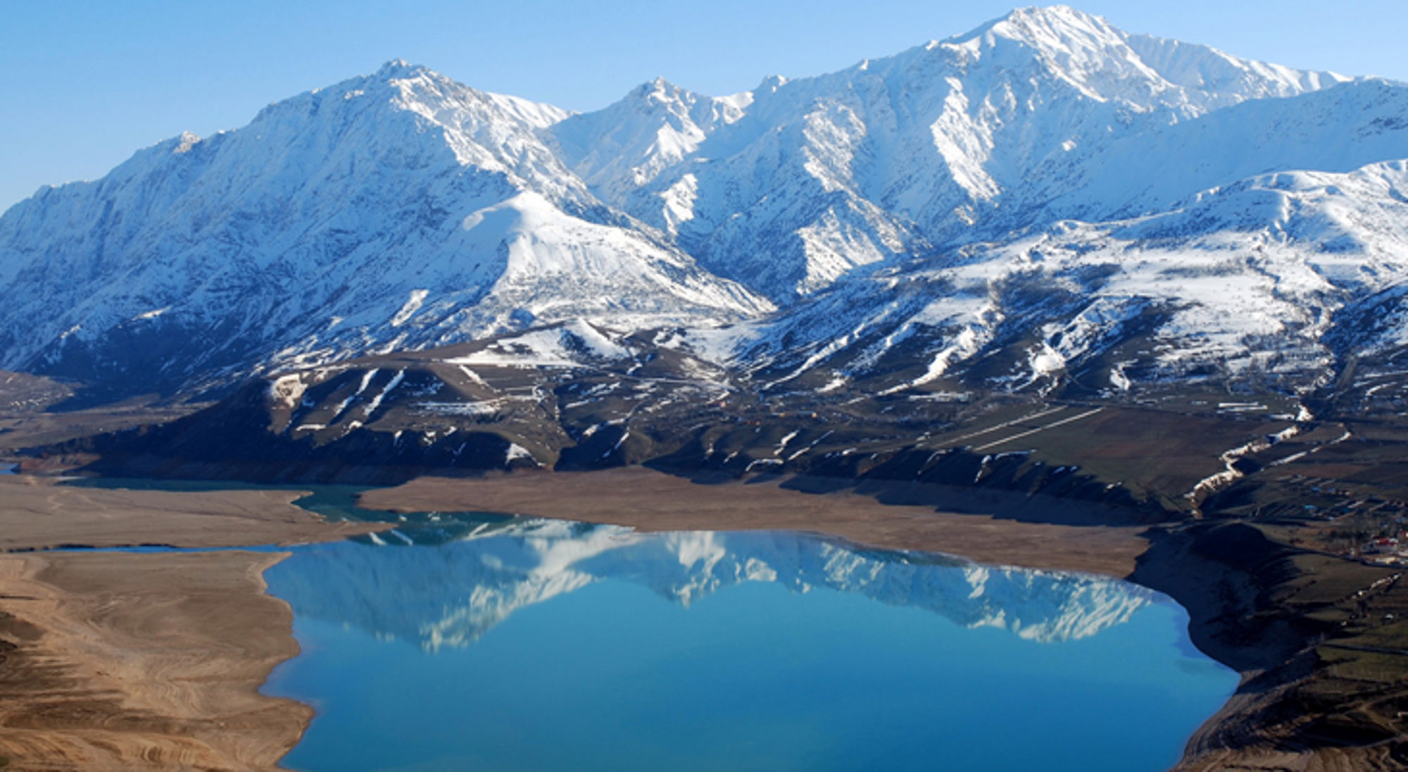 Besneeuwde bergketen met turquoise meer en spiegeling in het water.