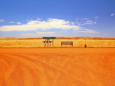 Rode zandweg met richtingborden naar Tom Price en Karratha in West-Australië.