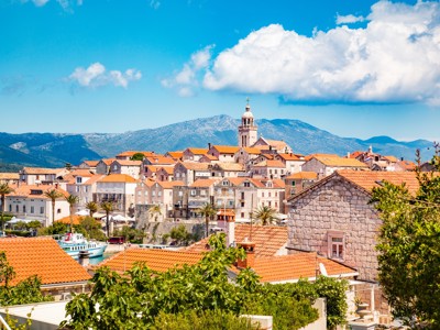 Uitzicht op het historische Korčula met rode daken, klokkentoren en bergen op de achtergrond.