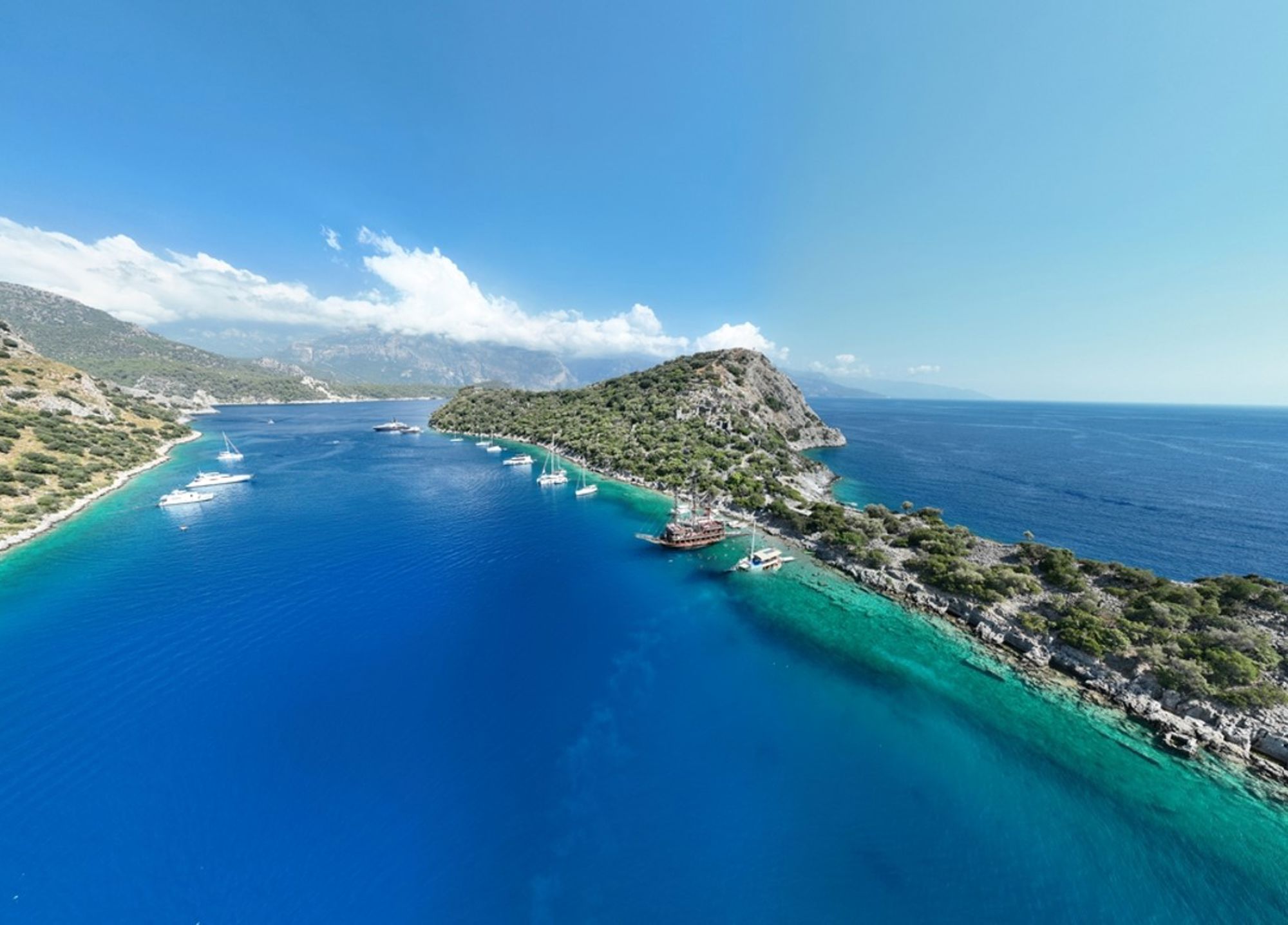 Turquoise baai met zeilboten langs een rotsachtige kust in Turkije.