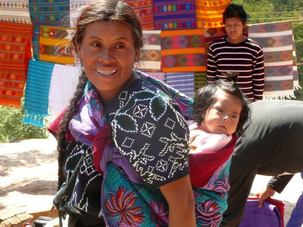 Vrouw met baby op de rug bij kleurrijke textielmarkt tijdens groepsrondreis Guatemala en Copán.