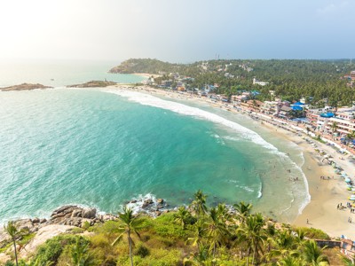Panoramisch uitzicht op het strand van Kovalam in Zuid-India, met palmbomen, zee en strandpromenade.