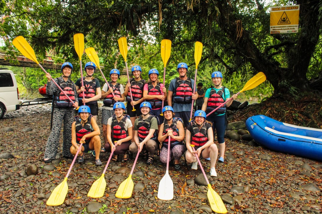 Groep reizigers klaar voor wildwaterraften in Costa Rica, met helmen, zwemvesten en peddels bij de rivier.