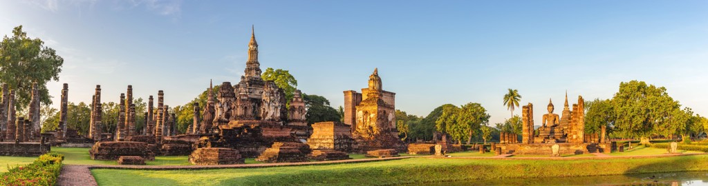 Historisch tempelcomplex in Sukhothai, Thailand, met Boeddhabeeld en ruïnes bij zonsondergang.