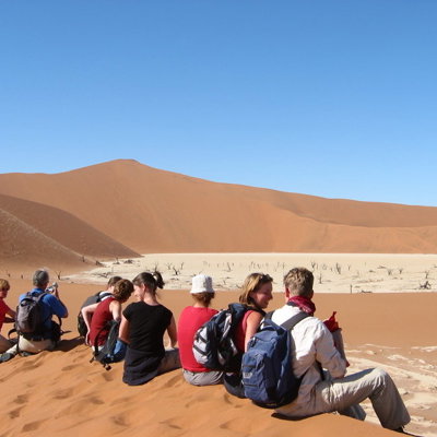 Groepsrondreis Namibië: reizigers rusten op een zandduin met uitzicht op Deadvlei en rode duinen.