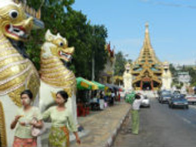 Straatbeeld in Yangon met gouden tempelpoort en mythische leeuwenbeelden langs de weg.