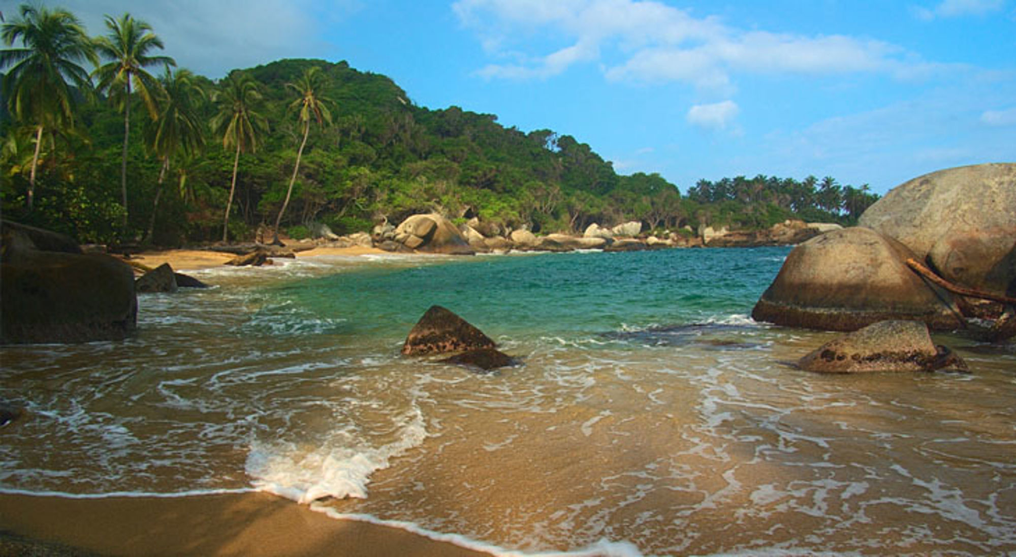 Tayrona Nationaal Park Tropisch strand in Colombia met palmbomen, granieten rotsen en helderblauw zeewater.