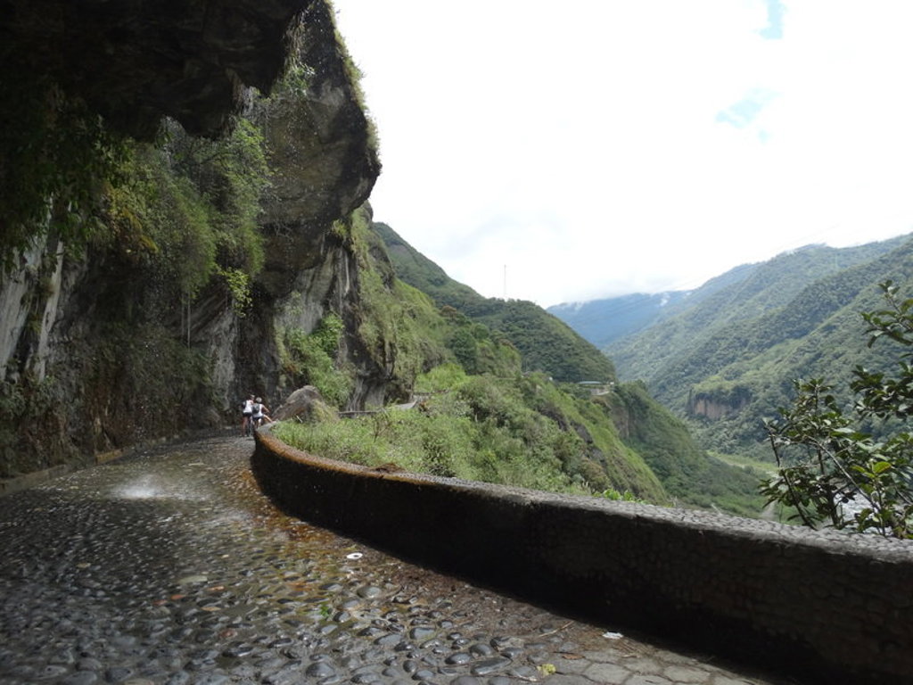 Wandelaars op smal bergpad langs een steile rotswand met uitzicht op groene vallei in Ecuador.