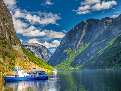 Fjordcruise in Scandinavië met boot tussen steile bergen en groen beboste hellingen onder blauwe lucht.
