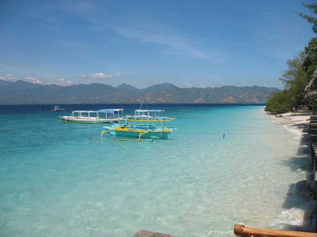 Traditionele boten in helderblauw water bij een wit zandstrand tijdens rondreis Bali en Lombok.