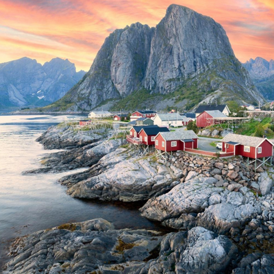 Rode vissershuisjes aan de kust van de Lofoten in Noorwegen, met bergen en zonsondergang op de achtergrond.