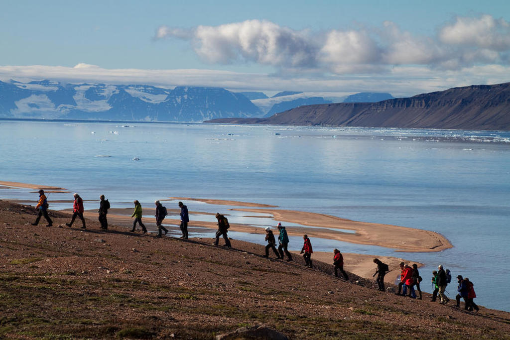 Wandelaars langs de kust bij Oost-Groenland tijdens een zeilreis, met fjord en besneeuwde bergen op de achtergrond.