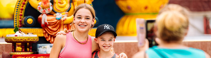 Kinderen poseren lachend voor een tempelbeeld tijdens een familieavontuur met Sawadee.