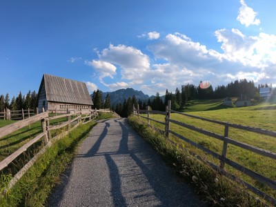 Landweg langs houten hekken en een berghut in de bergen van Zuidoost-Europa onder een blauwe lucht.