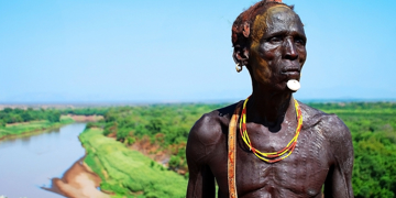 Portret van een man met traditionele sieraden bij een rivierlandschap in Ethiopië.