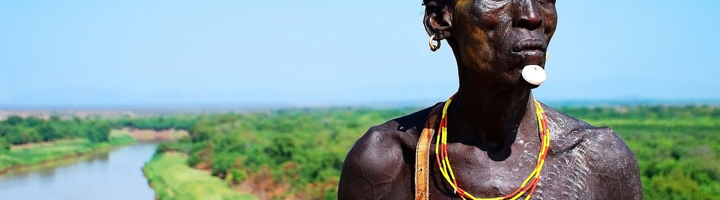 Portret van een man met traditionele sieraden bij een rivierlandschap in Ethiopië.