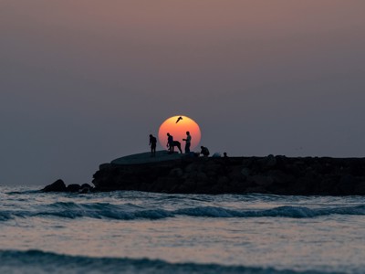 Zonsondergang aan de kust van Oman met silhouetten op een rotsige pier en golven op zee.