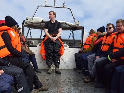 Groep reizigers in oranje reddingsvesten op een boot tijdens een excursie in IJsland.