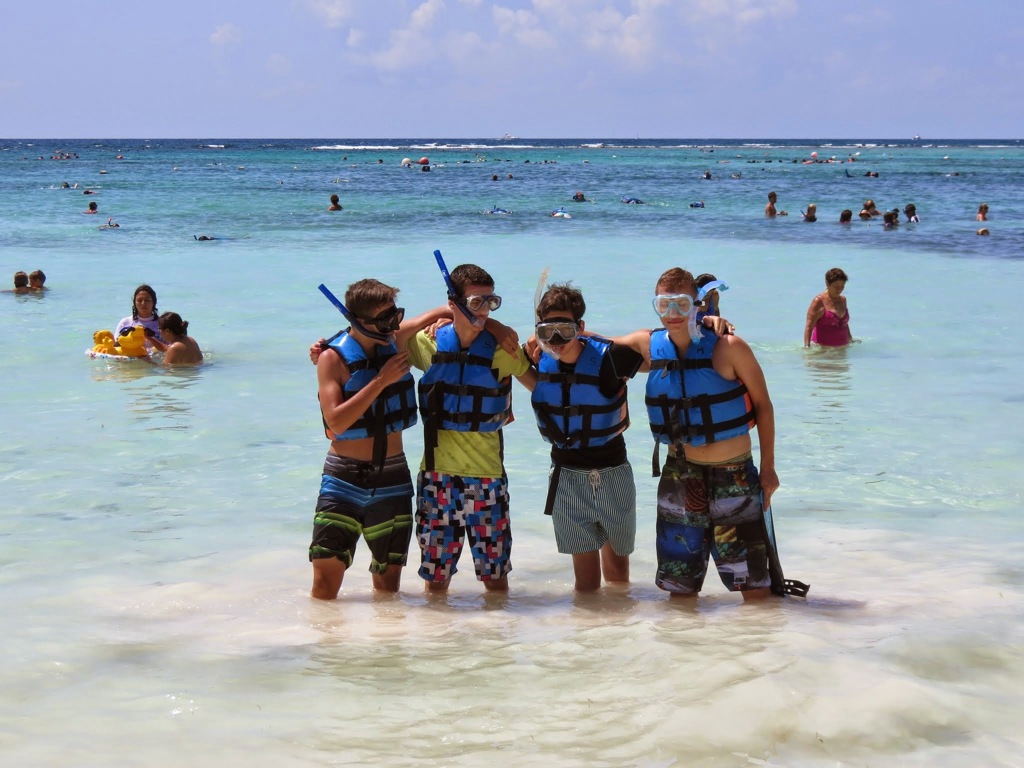 Tieners met snorkelsets en zwemvesten poseren in ondiep zeewater tijdens een familiereis in Mexico.