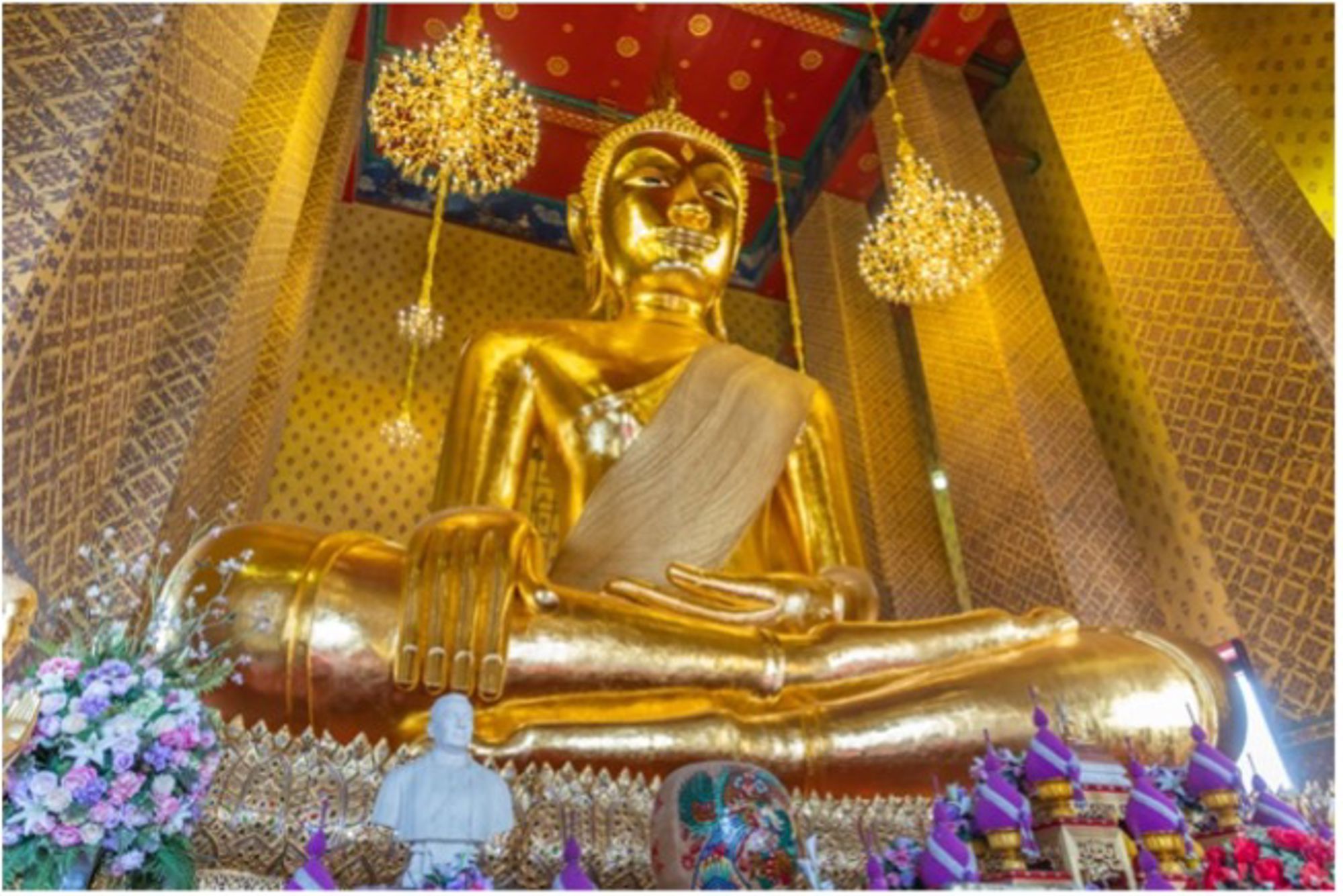 Gouden liggende Boeddha in een tempel, omringd door decoraties en kroonluchters.