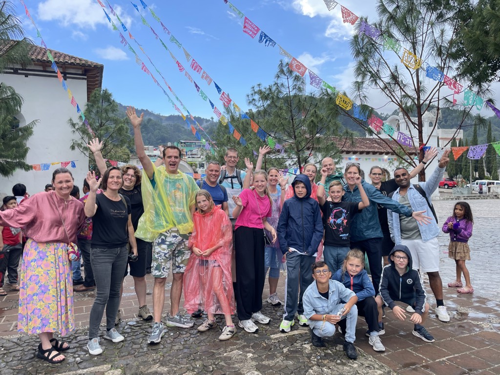 Groepsfoto van gezinnen tijdens familiereis Mexico op een plein met kleurrijke vlaggetjes en bergen op de achtergrond.