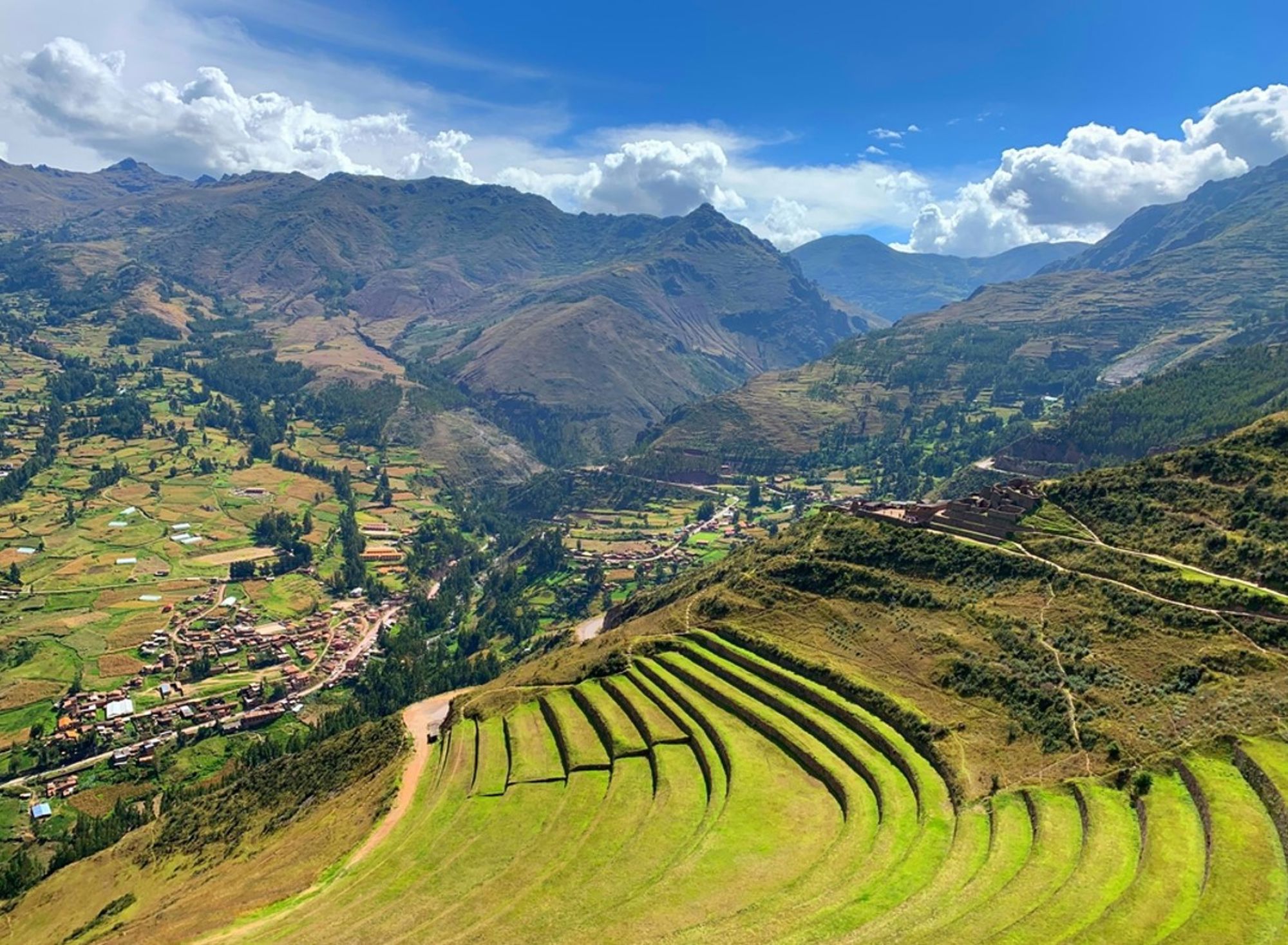 Groene terrassen van Pisac in de Heilige Vallei bij Cusco, Peru, met berglandschap en dorp in de verte.