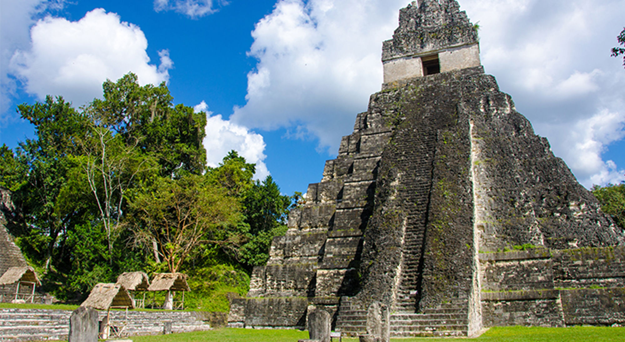 Maya-tempel tussen het groen bij Tikal, Guatemala, onder een blauwe lucht met wolken.