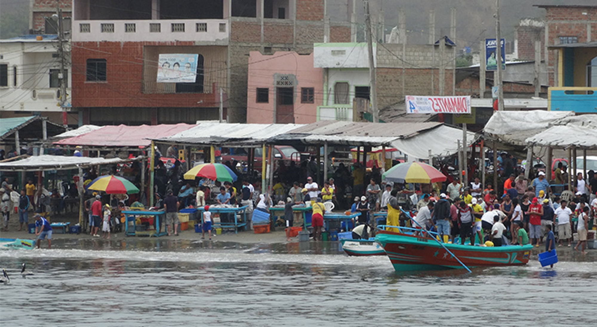 Boten in Ecuador Drukke vismarkt aan de waterkant met kleurrijke parasols en vissersboot in de voorgrond.