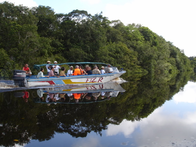 Boottocht met reizigers over een rustige rivier in Kalimantan, met spiegeling van het regenwoud in het water.
