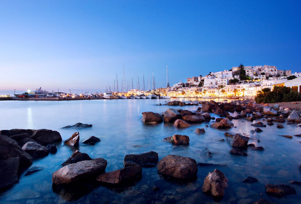 Avondzicht op de haven van Naxos met witte huizen, zeilboten en rotsachtige kust, Griekenland.