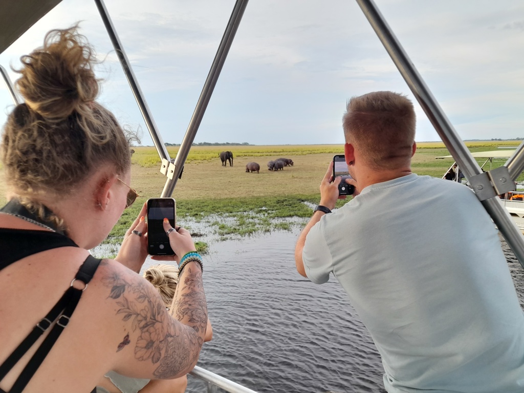 Reizigers tijdens 22-35ers reis Zuidelijk Afrika fotograferen nijlpaarden en olifant vanaf een boot.