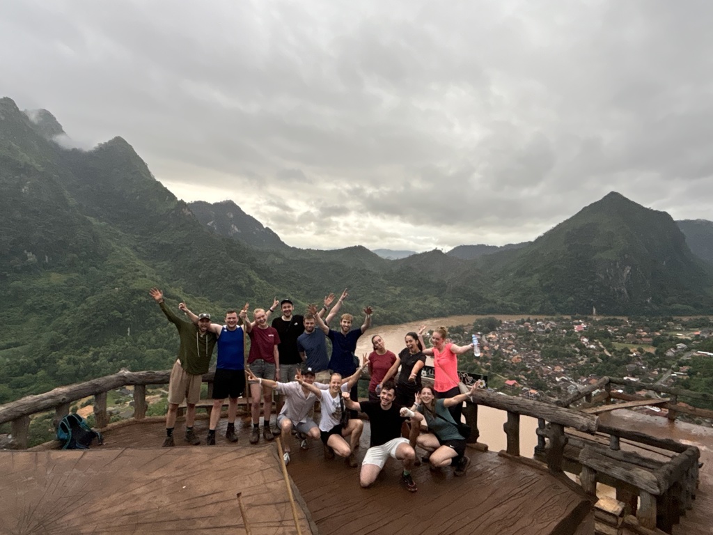 Reisgroep op uitkijkpunt met uitzicht op bergen, rivier en dorp tijdens 22-35ers reis Thailand, Laos en Cambodja.