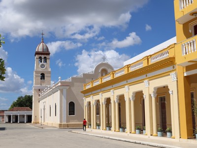 Straat in Trinidad, Cuba met kleurrijke arcades en kerk met klokkentoren onder een blauwe lucht.