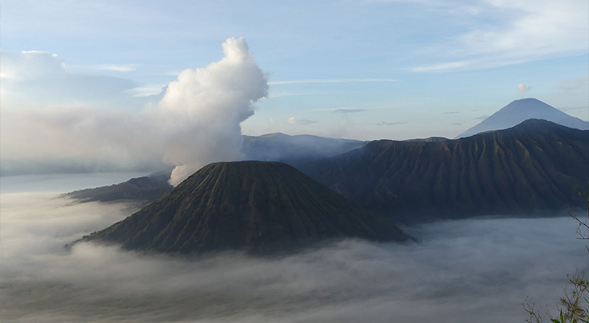 Rokende vulkaan in berglandschap boven een zee van mist bij zonsopkomst.