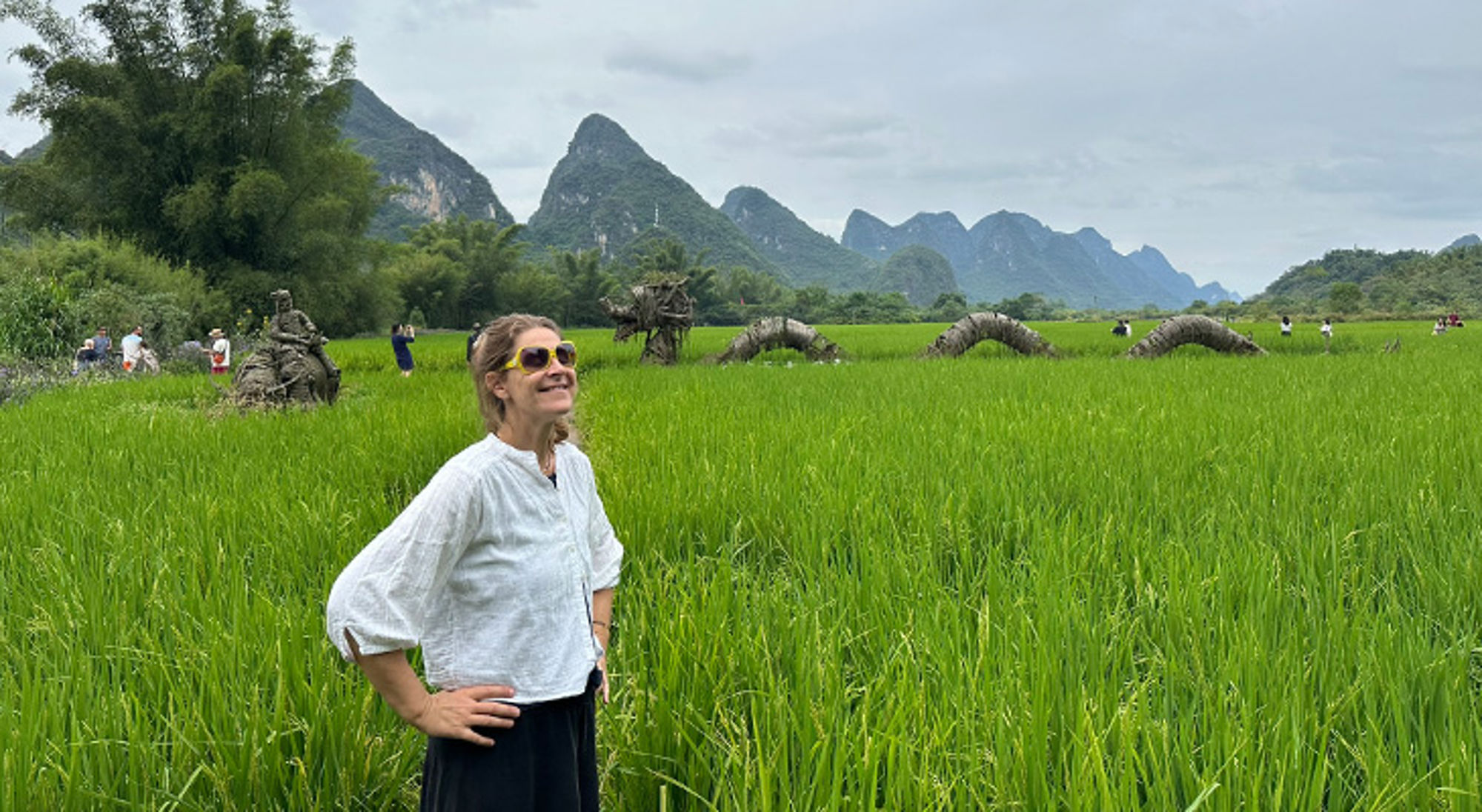 Tessa in China Vrouw in groen rijstveld met karstbergen op de achtergrond.