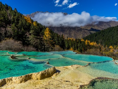 Turquoise kalksteenterrassen bij Huanglong met dennenbos en bergen in de wolken, China.