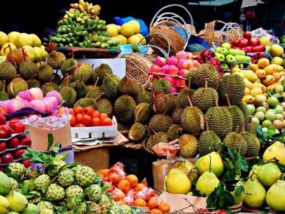Kleurrijke fruitmarkt in Thailand met durians, mango’s, appels en citrusvruchten op marktkramen.