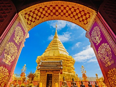 Gouden boeddhistische pagode gezien door een rijk versierde tempelboog in Thailand.