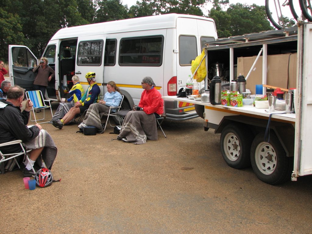 Pauze tijdens fietsvakantie in Zuid-Afrika met groep fietsers bij supportbus en trailer met koffie en snacks.