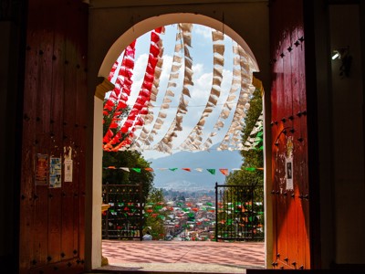Uitzicht op stad en bergen door een poort met rood-wit-groene vlaggetjes in Mexico.