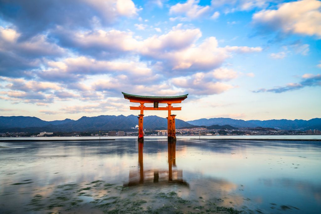 Rode torii-poort in zee bij Miyajima, Japan, met bergen op de achtergrond tijdens zonsondergang.