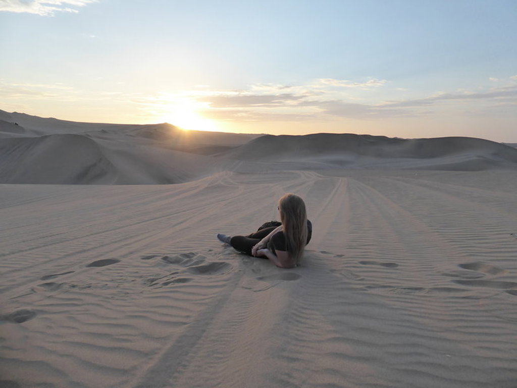 Reiziger rust in de zandduinen van Peru bij zonsondergang tijdens een 22-35ers groepsrondreis.