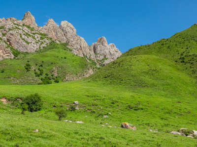 Groene heuvels en ruige bergtoppen langs de Zijderoute met de trein, onder een helderblauwe lucht.
