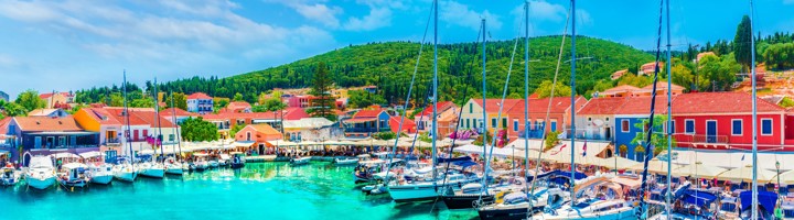 Jachthaven van Fiskardo met zeilboten en kleurrijke huizen aan turquoise water op Kefalonia, Griekenland.
